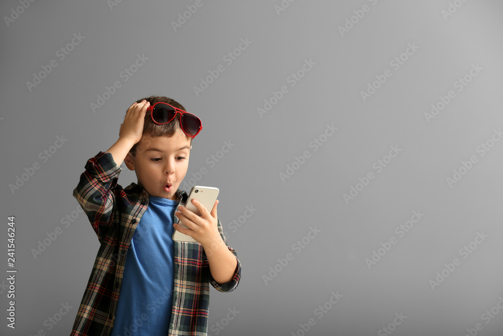 Emotional little boy playing with smartphone on grey background - obrazy, fototapety, plakaty 