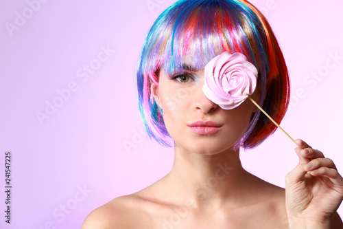 Beautiful young woman with sweet lollipop and wig on color background