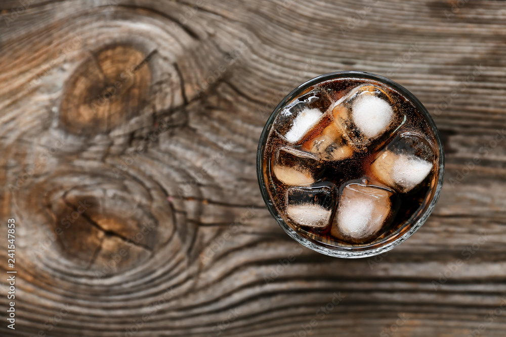 Glass of soda with ice on wooden table