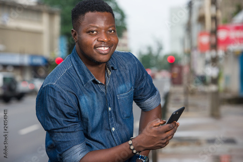 smiling man sitting outside and holding his phone in his hands