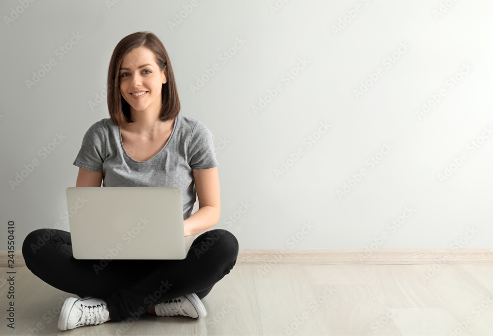 Young woman with laptop sitting on floor near light wall Young woman with laptop sitting on floor near light wall