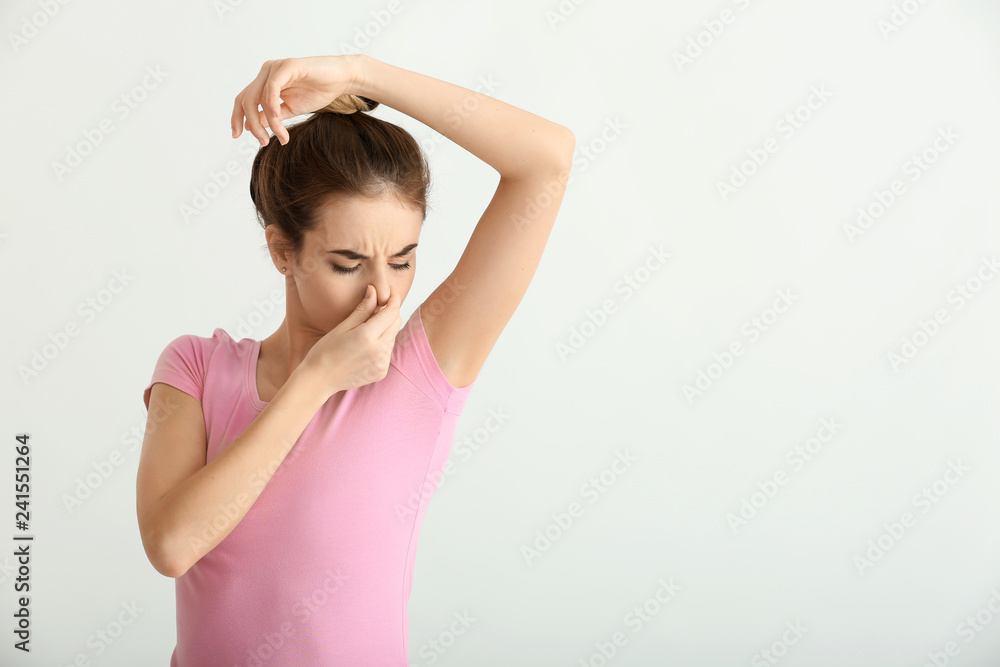 Beautiful young woman feeling smell of sweat on light background. Concept of using deodorant Beautiful young woman feeling smell of sweat on light background. Concept of using deodorant