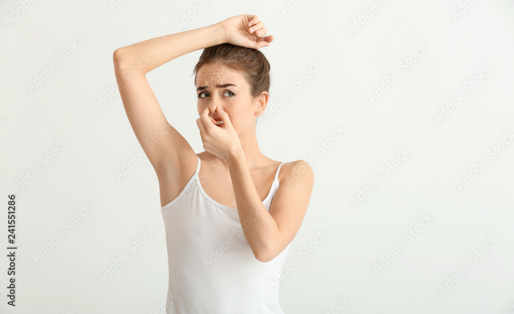 Beautiful young woman feeling smell of sweat on light background. Concept of using deodorant Beautiful young woman feeling smell of sweat on light background. Concept of using deodorant