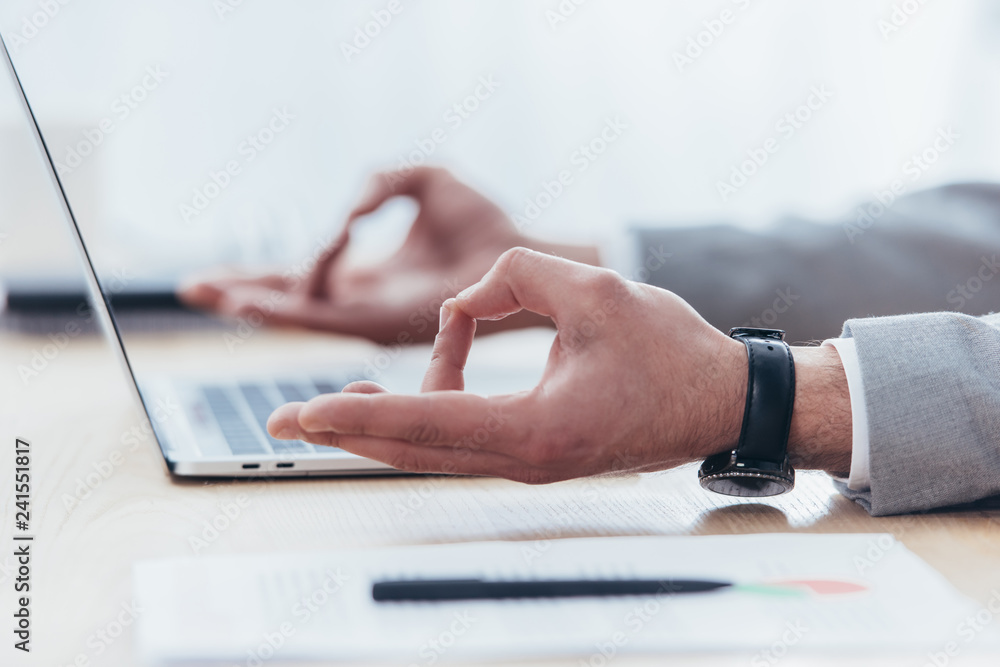 Fototapeta premium close-up partial view of businessman meditating while working with laptop in office