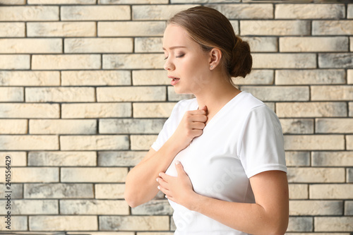 Photos Young woman having asthma attack against brick wall