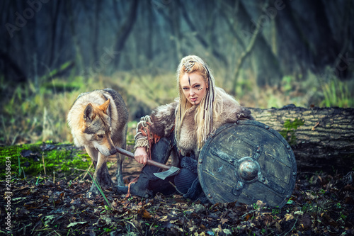 Fototapeta Viking warrior woman holding shield and ax  alone in woods with wolf next to her