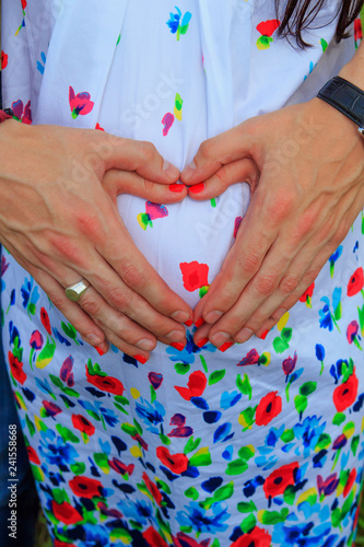 A couple making a heart shape on the pregnant belly with their hands. Concept of pregnancy,