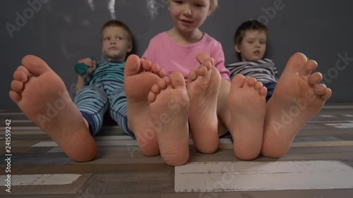 Cheerful children in multi-colored striped clothes are engaged in gymnastics with dumbbells. Legs and feet close-up. Children enjoy winter vacations together. Concept of family fitness classes.