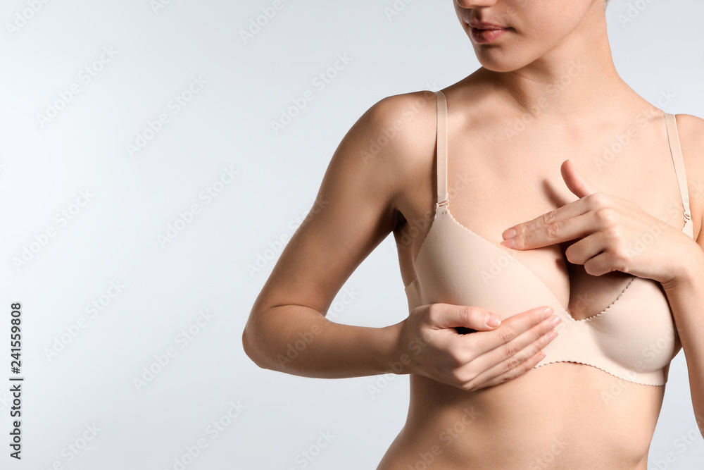 Obraz premium Young woman checking her breast on light background. Cancer awareness concept
