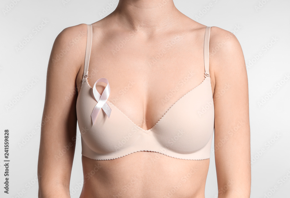 Young woman with beautiful breast and pink ribbon on light background. Cancer awareness concept