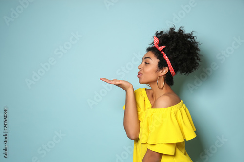 Portrait of young African-American woman blowing kiss on color background