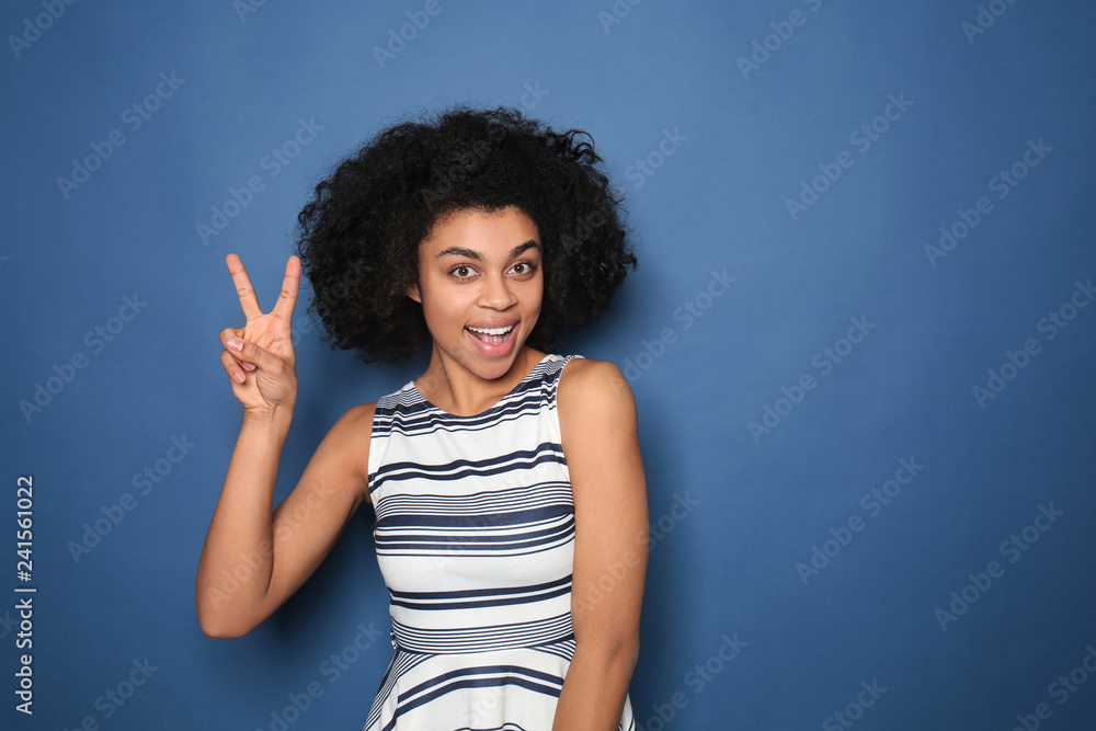 Portrait of young African-American woman showing victory gesture on color background Portrait of young African-American woman showing victory gesture on color background