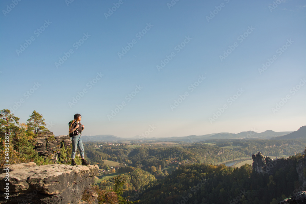 Young woman traveler with baclpack stand on the cliff in mountains