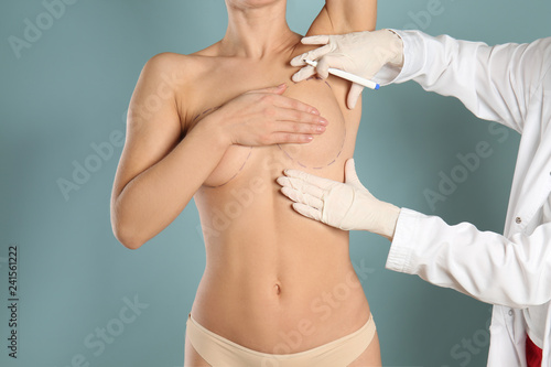 Doctor drawing marks on female breast before cosmetic surgery operation against color background photo
