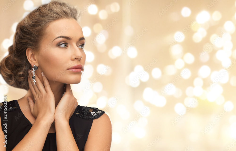 Obraz premium jewelry, people and luxury concept - beautiful young woman wearing diamond earrings over beige background and festive lights