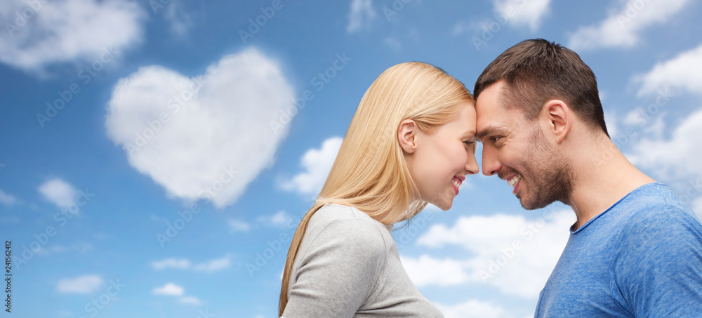 love, valentines day and people concept - smiling couple standing forehead to forehead over blue sky and heart shaped cloud background love, valentines day and people concept - smiling couple standing forehead to forehead over blue sky and heart shaped cloud background