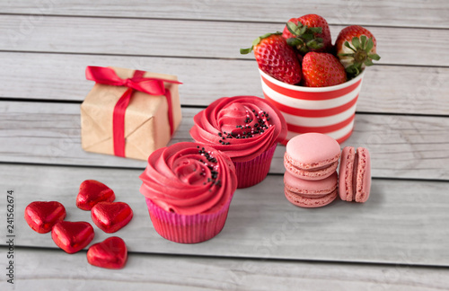 Fototapeta Naklejka Na Ścianę i Meble -  valentines day and sweets concept - close up of frosted cupcakes, red heart shaped chocolate candies, macarons, strawberries and gift box
