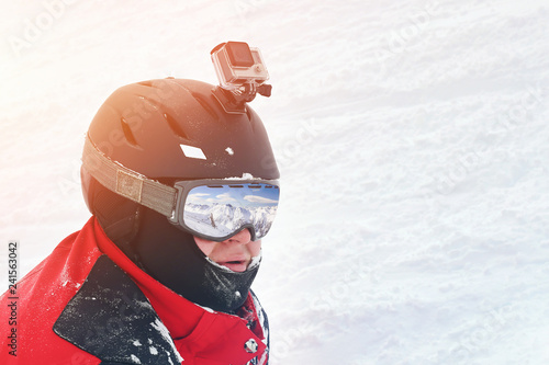 Snowboarder or skier portrait in sport goggles and protection helmet with mounted action camera and ski slope on background. Exreme winter sport outdoor activities photo