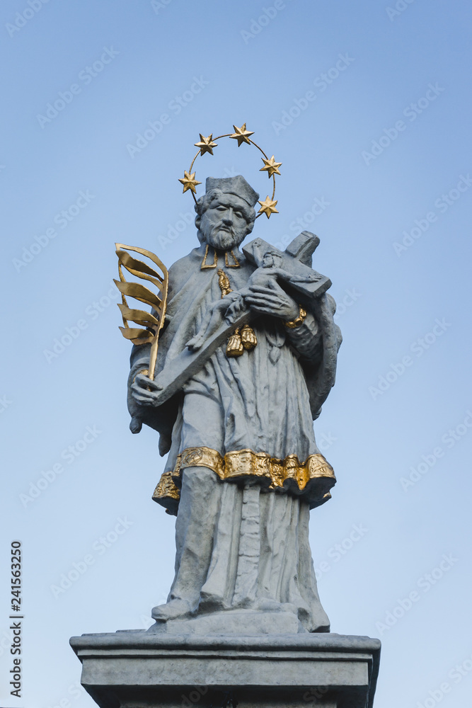 Obraz premium Statue of Saint John of Nepomuk in Olesno, Poland with gold elements: palm of martyrdom, halo of five stars, robes and crucifix cross with Jesus. St John is the Patron Saint of Bohemia & Confession.
