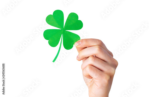 fortune, luck and st patricks day concept - hand holding green paper shamrock over gray background