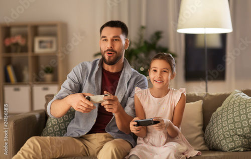 family, gaming and entertainment concept - happy father and little daughter with gamepads playing video game at home photo