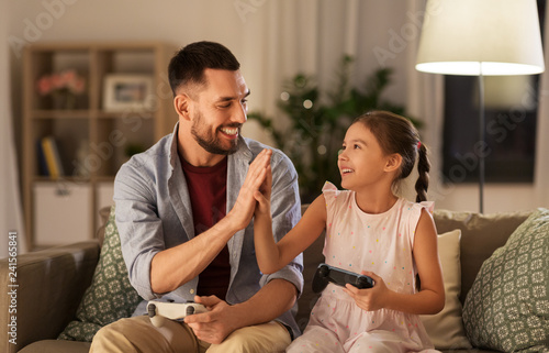 Fototapeta Naklejka Na Ścianę i Meble -  family, gaming and entertainment concept - happy father and little daughter with gamepads playing video game at home