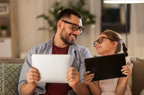family, fatherhood and technology concept - happy father and daughter in glasses with tablet pc computers at home
