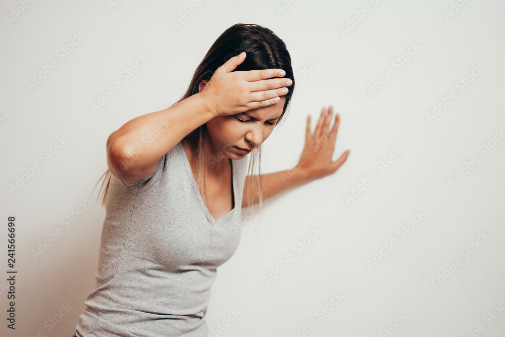 Woman suffering from dizziness with difficulty standing up while leaning on wall Woman suffering from dizziness with difficulty standing up while leaning on wall