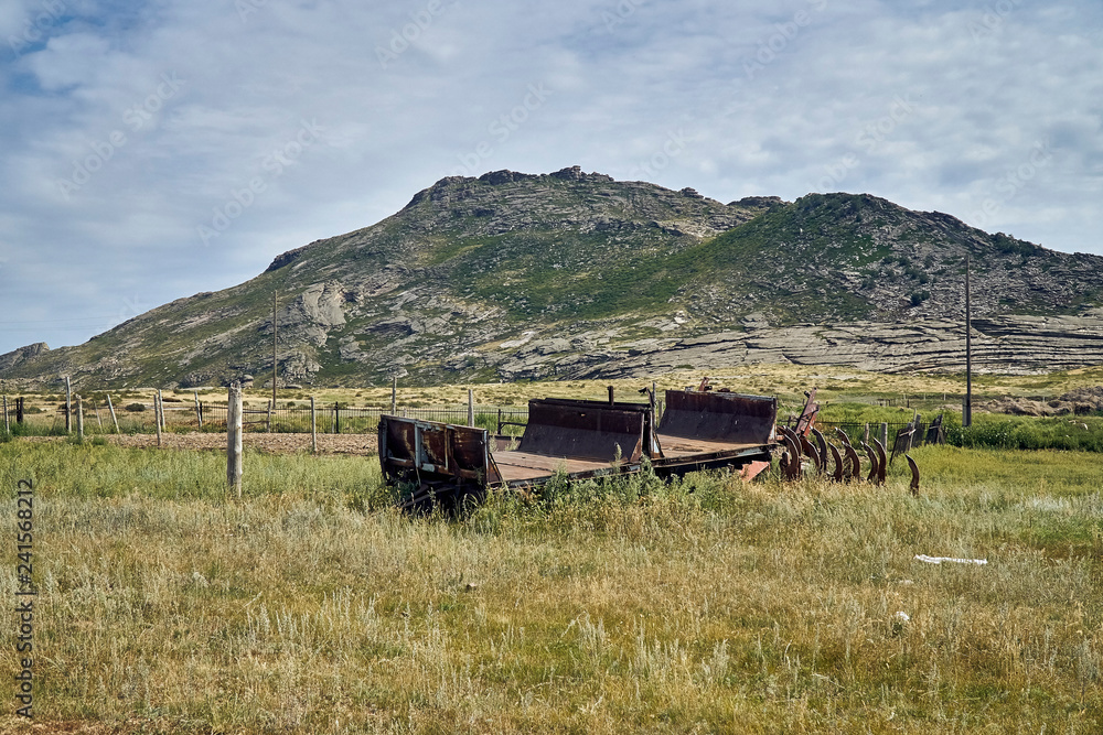 Obraz premium The old Soviet auto and agricultural machinery abandoned in the steppe not far from Sartymbet village, stone mountains 