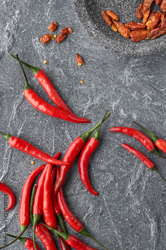 Close-up on red hot chili peppers, fresh and dry, on grey stone, flat lay