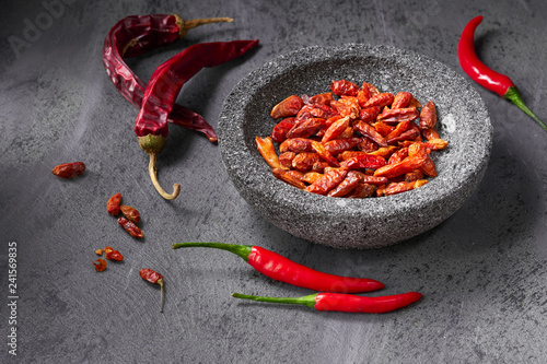 Closeup on fresh hot chili peppers on dark textured table and dry ones in stone bowl