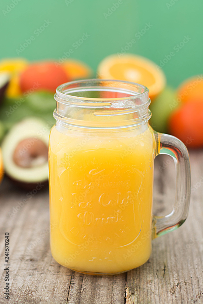 Orange juice and carrot juice, in the glass jar. Green background. Rustic wooden table. Healthy, vegan food and drinks. Orange juice and carrot juice, in the glass jar. Green background. Rustic wooden table. Healthy, vegan food and drinks.