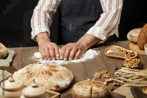 Hands of male chef cook working with dough, surrounded by bread and long loafs from whole wheat flour. Bakery concept. Homemade bakery concept