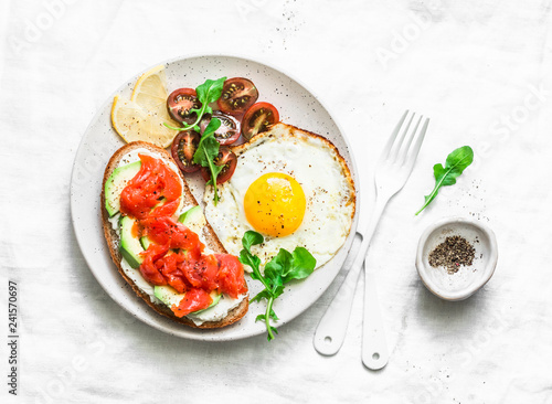 Whole grain bread, cream cheese, avocado, smoked salmon sandwich and fried egg - delicious breakfast, snack, brunch on a light background, top view