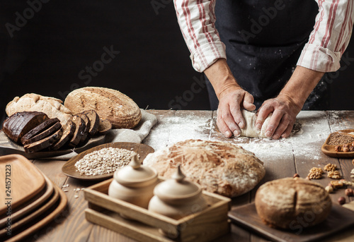 Hands of caucasian man prepares pastry by himself, close up. Man kneads dough on wooden counter with flour and rolling pin, baking organic bread or delicious bun.