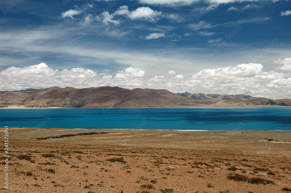 Lake with turquoise water in Tibet against the backdrop of mountains and clouds
