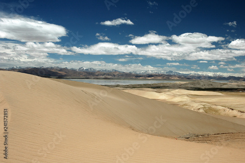 Sandy hills, lake, blue sky and clouds in a Tibetan landscape