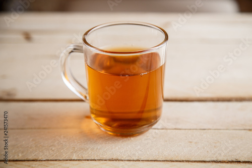Transparent cup with a hot drink on light wooden background . View from above.