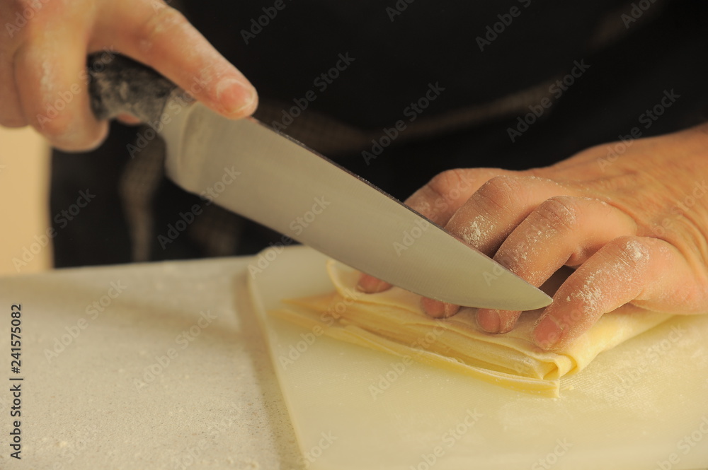 Cutting of noodles roll on cutting board by hands close up Cutting of noodles roll on cutting board by hands close up