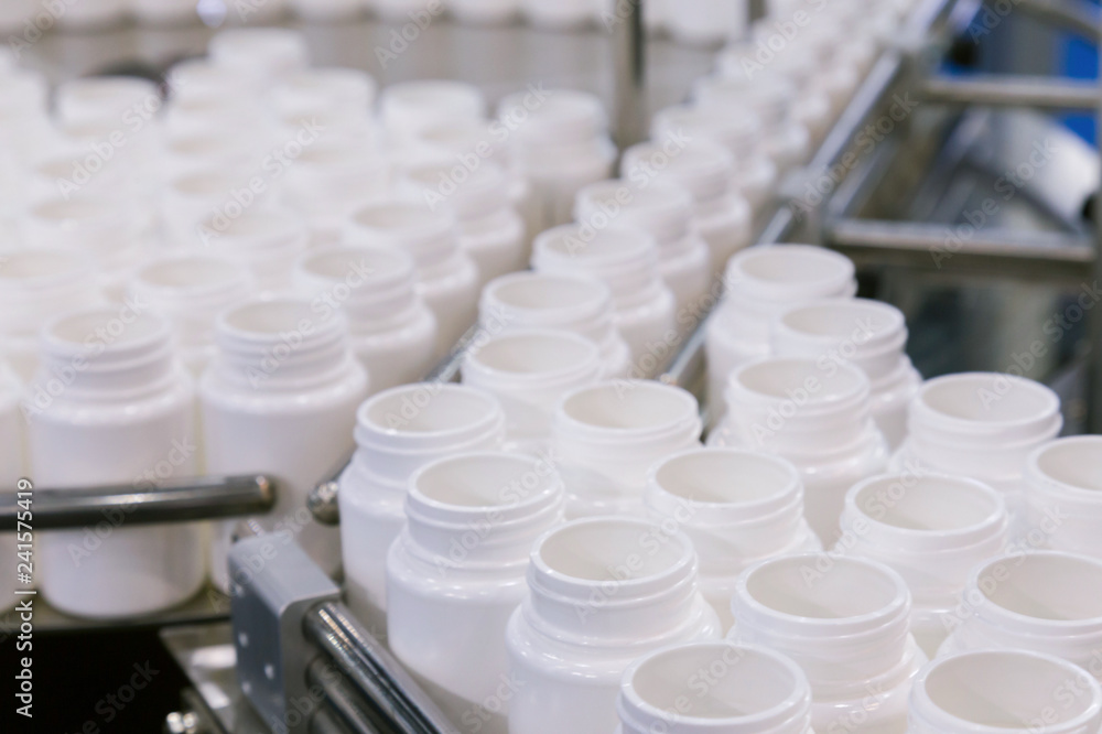 white plastic bottle on the production line of the conveyor at filling machine in the medical factory. selective focus. white plastic bottle on the production line of the conveyor at filling machine in the medical factory. selective focus.