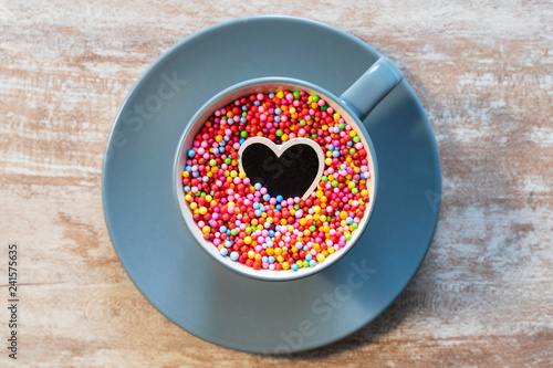 Cozy wooden background, with a blue cup with colored balls inside and a black heart, love concept, for Valentine's Day, Mother's Day, Father's Day, Christmas, holidays.