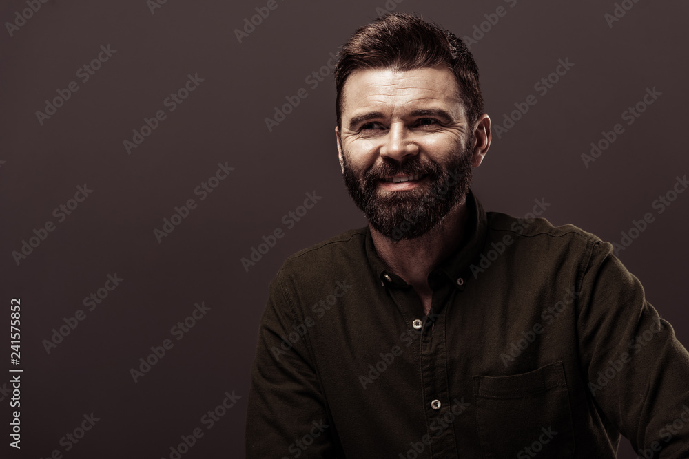 handsome bearded man in brown shirt smiling isolated on brown