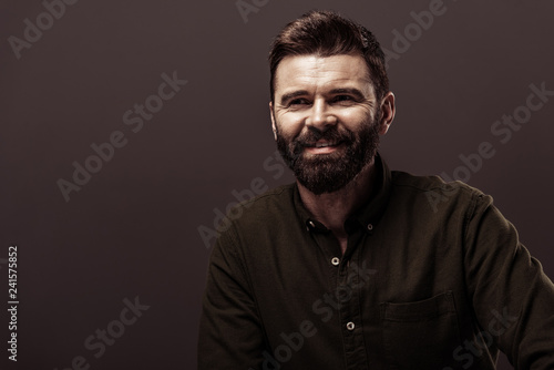 handsome bearded man in brown shirt smiling isolated on brown