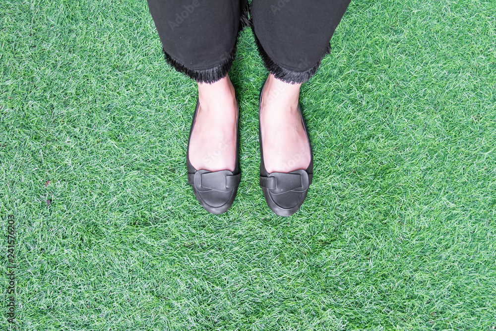Woman feet wearing black shoes on a green grass background.