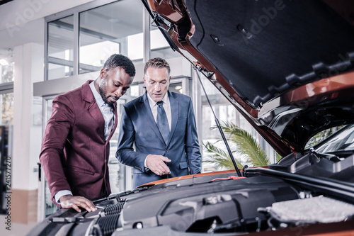 Businessmen standing near open front trunk thinking about buying car