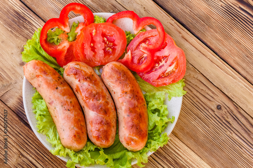 Ceramic plate with grilled sausages, sliced tomatoes and lettuce leaves on wooden table. Top view Ceramic plate with grilled sausages, sliced tomatoes and lettuce leaves on wooden table. Top view