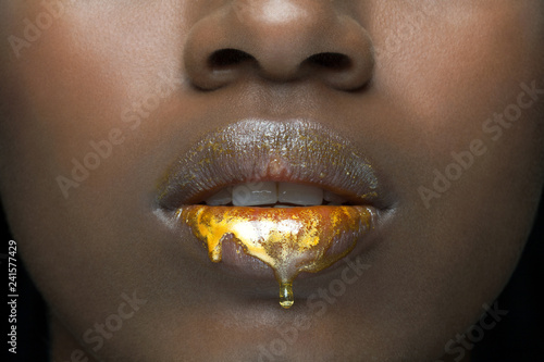 Close up of a beautiful, young, black woman's lips with golden, liquid make up dripping down her lips.