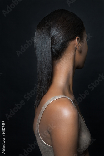 Profile of a beautiful, young, black woman facing away from the camera with long, black hair and shiny skin.