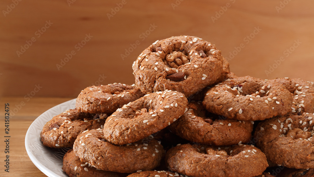 Homemade oatmeal cookies with nuts, chocolate chips and sesame. On a wooden background.
