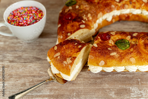 King's cake made by hand in the oven, on a cozy wooden base, and a cup with colorful chocolate topping.